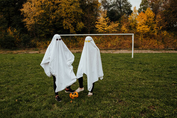 girls in ghost costumes for Halloween, football field in autumn

 