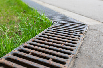 A rusted metal sewer grate along a paved walkway. The edge of the pavement. Close-up