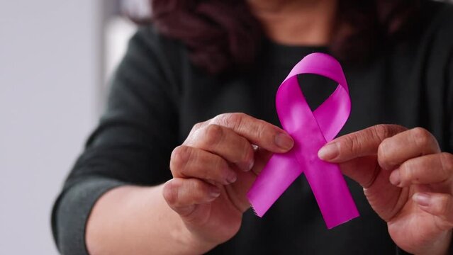 video of a woman's hands showing a pink or purple ribbon bow as a symbol of the fight against breast cancer (other types of cancer). World Cancer Awareness Month and World Cancer Day concept.