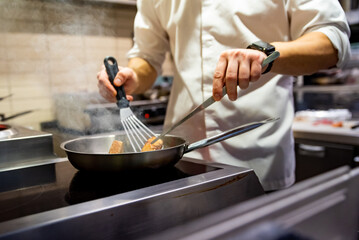 man chef cooking fried salmon fish in frying pan on kitchen