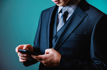 Smart young man in luxury black suit using smartphone on dark brown background.