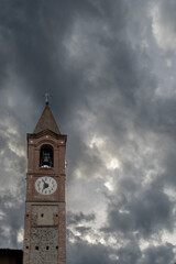 Ancient church tower in Almese, Piedmont, Italy. Bell tower with a cross and a clock.