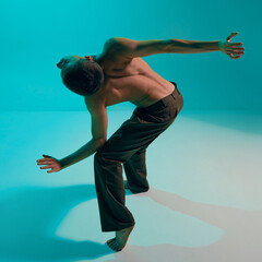 Contemporary dance style. Young man, professional contemp dancer, performing, dancing over blue,...