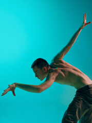 Contemporary dance style. Young shirtless, muscular man dancing over blue, cyan studio background. Well-coordinated movements. Concept of art, body aesthetics, motion, action, inspiration, feelings