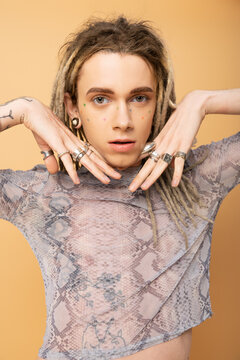 Portrait of tattooed queer person with rings on fingers looking at camera isolated on yellow.