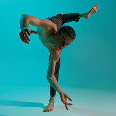 Bottom view. Contemporary dance style. Young flexible, shirtless man dancing over blue, cyan studio...