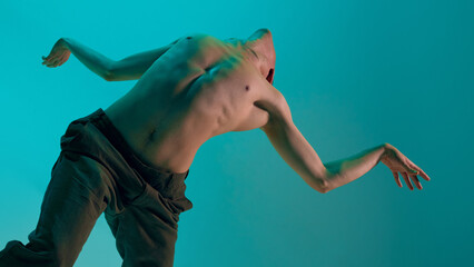 Bottom view. Contemporary dance style. Young flexible man dancing experimental dance over blue, cyan studio background. Feelings. Concept of art, body aesthetics, motion, action, inspiration.