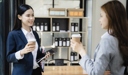 Female colleague during work break standing holding coffee mugs in work area smiling various business team talking joyfully enjoying conversation friendly relations in the office.