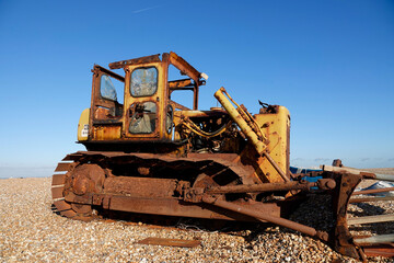 Abandoned yellow tractor on Dungeness beach under clear blue sky