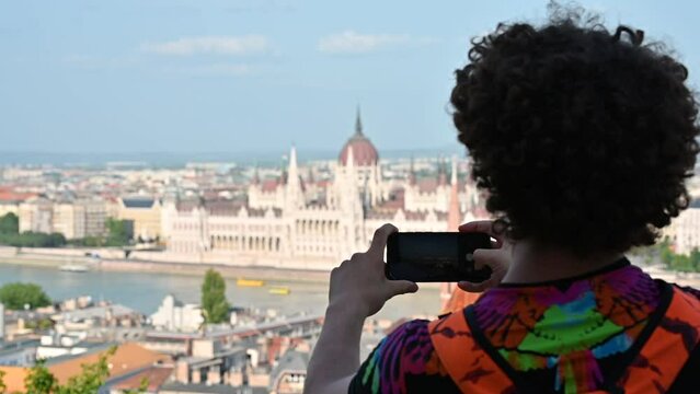 Budapest,Hungary,August 2022. Slow motion footage with a young Caucasian man taking a photo with his cellphone to the blurry aerial view of the parliament. Beautiful summer day.