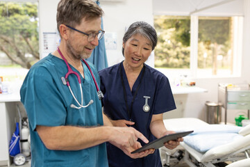 Man and woman health care workers  standing next to each other looking at a tablet in the clinic