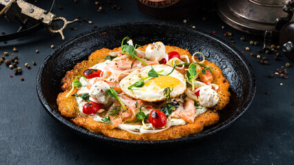 Obraz na płótnie Canvas Fried big potato pancake with salmon fish, tomatoes, egg, onion, herbs and sour cream in a frying pan.