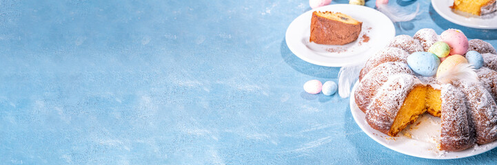 Traditional cake for Easter. Chocolate and vanilla Easter round cake with chocolate and sugar powder sprinkles, colorful Easter eggs, spring flowers, on a blue background copy space
