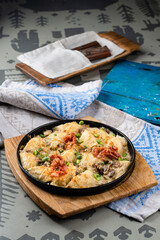 Lunch baked meat dumplings with cheese and bacon, tomatoes and onions in a cast iron pan.