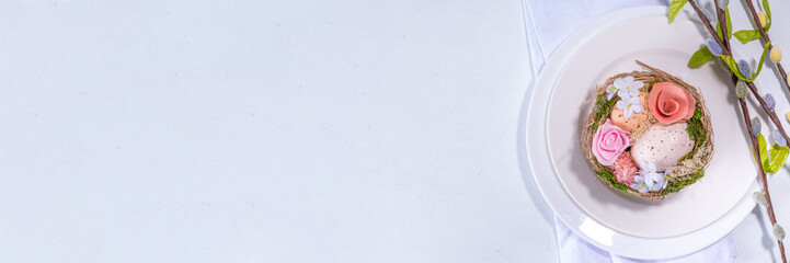 Easter table setting. Festive spring holiday cutlery set, with plate, wine glass, knife, fork, with Easter decor egg nest, willow flower branches, white sunny table background copy space top view