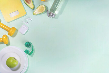 Spring slim and fitness, active living concept. Small yellow dumbbells, bottle of water, sports shoes, scales, salad, fresh vegetables and fruits on a light green background, top view copy space