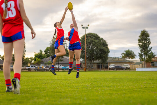 two female footy players stretching up to tap the ball away