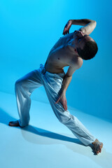 Contemporary dance style. Young artistic man dancing contemp, experimental dance over blue studio...