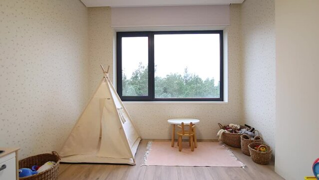 Motorized roller blinds in the children's room. Automatic roller shades on the window in the interior of child's room. Trees outside. Electric sunscreen curtains for home. Playhouse and toys there.