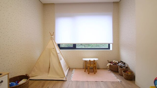 Motorized roller blinds in the children's room. Automatic roller shades on the window in the interior of child's room. Trees outside. Electric sunscreen curtains for home. Playhouse and toys there.