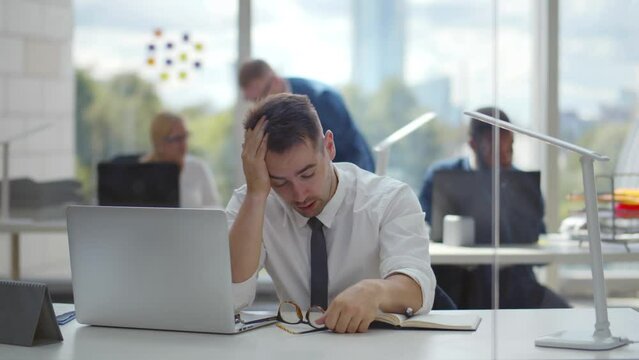 Businessman taking off his glasses feeling tired, working online on laptop 
