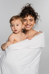 happy mother and toddler baby girl covered in duvet isolated on grey.