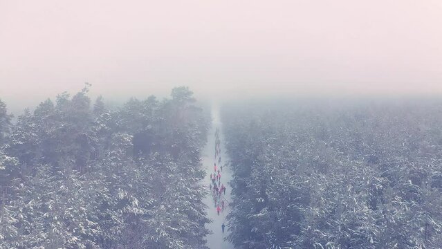 High altitude drone flight above runners on the snowy path during winter run in foggy forest