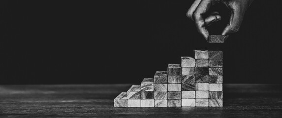 Hand placing wooden block tower stack in pyramid stair step with caution to prevent collapse or...