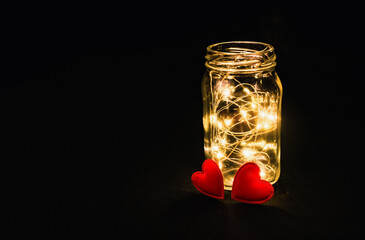 The warmth of two hearts. Atmospheric photo of glowing red hearts in glass. Black background.
