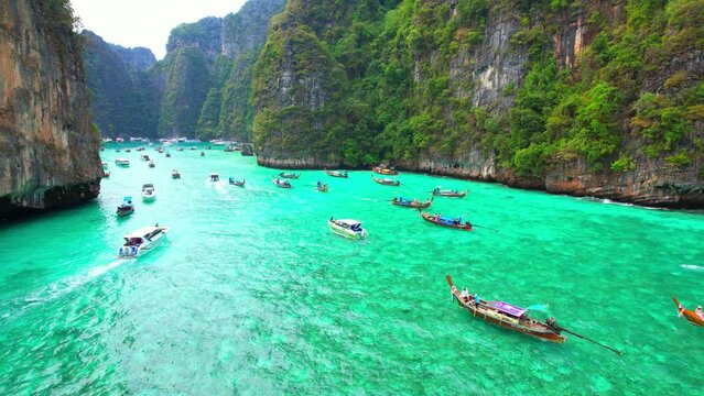 Aerial view over tropical sea, beautiful waters look more green than blue, limestone cliffs which have impressive vegetation. Long-tailed boats and many tourists. Pileh lagoon, Krabi, Thailand. 4K UHD