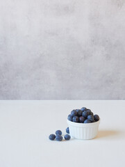 small bowl with fresh ripe blueberries placed on white table near gray wall