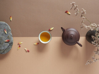 Top view of ceramic teapot and cup of hot drink placed on table near dried flowers in vase and stone with floral petals - obrazy, fototapety, plakaty
