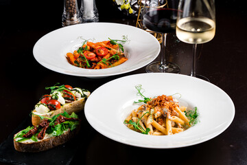 Italian food pasta Penne with porcini mushrooms and tomatoes in tomato sauce garnished with green peas and bruschettas with tomatoes, mozzarella, pesto sauce, sun-dried tomatoes and arugula.