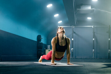Young fit woman in sportswear doing yoga at gym in upward facing dog pose.