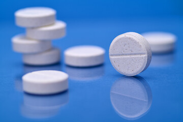 Stack of white pills to treat an ailment or relieve pain on blue background, medication prescribed by doctor to fight epidemic or virus