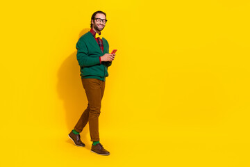 Fototapeta na wymiar Full length profile portrait of cheerful nice man hold telephone walk empty space isolated on yellow color background