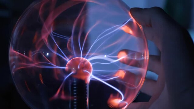 Scientist hand is touching electric plasma ball with luminous flames - physical experiment.