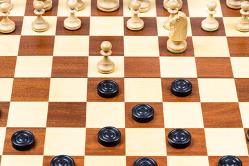 playing by different rules on the same board - black checkers and white chess figures on wooden...