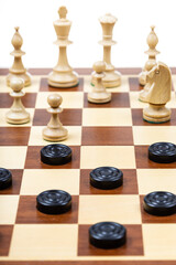 playing by different rules on the same board - black checkers and white chess figures on wooden chessboard, part of playfield with chess and checkers gaming on board (focus on front checkers disc)
