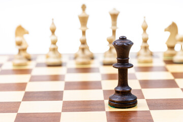black queen against white chess pieces in background on wooden chessboard close up (focus on queen)