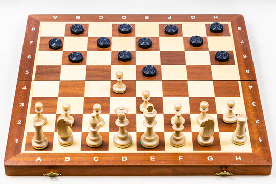 playing by different rules on the same board - black checkers and white chess figures on wooden chessboard, chessboard with first moves of chess and checkers (focus on center of board)