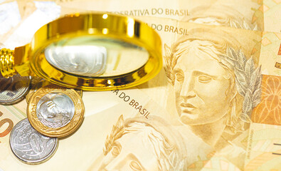 Notas do Real Brasileiro sobre uma mesa com uma lupa dourada na composição. Economia brasileira e...