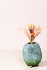 ceramic vase with bouquet of dried plants on light brown table with pink background with copyspace