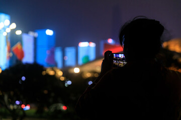 Fototapeta na wymiar A woman took a mobile phone to shoot a city light show. Shenzhen, China