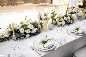 Wedding decorations. Served wedding table with decorative fresh white flowers and candles. Celebration details. flower composition roses plates and candles in candlesticks