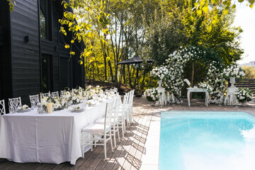 A general plan of a wedding decor from an arch decorated with fresh white flowers and a festive table for guests with a serving decorated with white flowers and various candles
