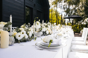 Wedding decorations. Served wedding table with decorative fresh white flowers and candles. Celebration details. flower composition roses plates and candles in candlesticks