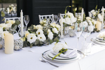 Wedding decorations. Served wedding table with decorative fresh white flowers and candles. Celebration details. flower composition roses plates and candles in candlesticks