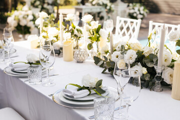 Wedding decorations. Served wedding table with decorative fresh white flowers and candles. Celebration details. flower composition roses plates and candles in candlesticks