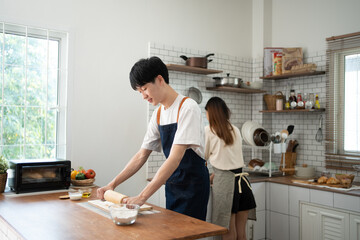 man in apron rolling out dough for homemade pastry, enjoying preparing biscuit cookies in modern light kitchen.